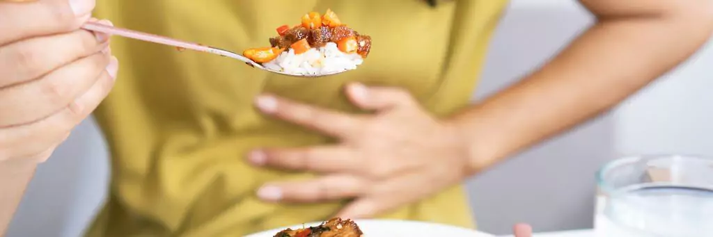 moça segurando colher de comida e com a outra mão na barriga
